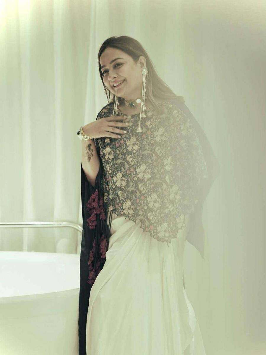 A client of Tanya Jain in an ivory drape with an embellished cape, against a pale curtain