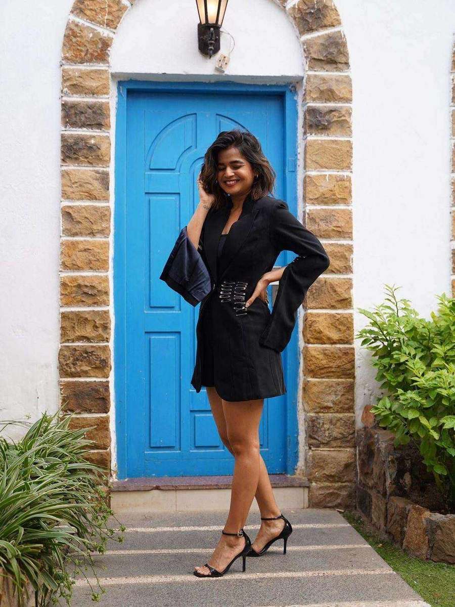 Suhani Shah, styled by Tanya Jain in the same look, leaning against the blue door frame
