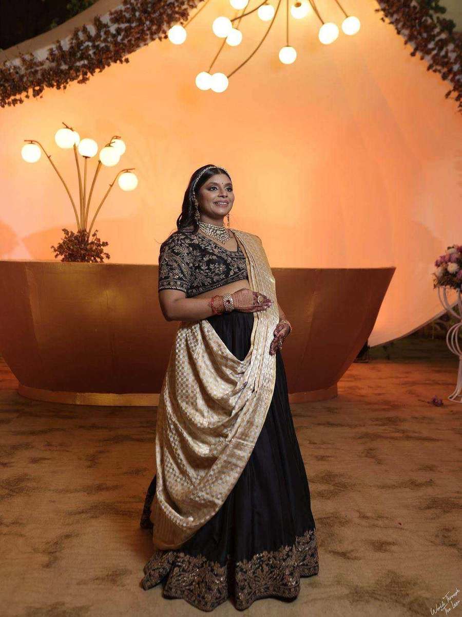 Tanya Jain in a black and gold saree, photographed beneath a lit installation